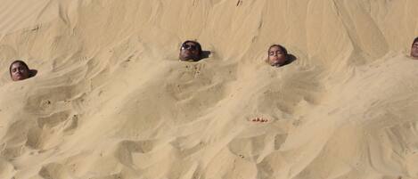 A large sand formation with people partially buried in it.