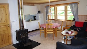 A cozy room with a wood stove, a dining table with chairs, a sofa, and a kitchen area with a microwave.