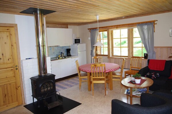 A cozy room with a wood stove, a dining table with chairs, a sofa, and a kitchen area with a microwave.