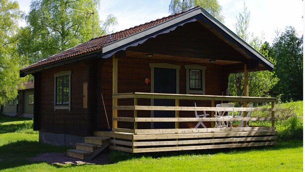 A small wooden cabin with a porch, steps leading up to the entrance, and a few chairs on the porch.