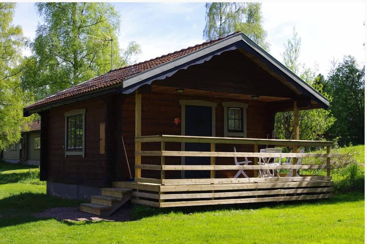A small wooden cabin with a porch, steps leading up to the entrance, and a few chairs on the porch.