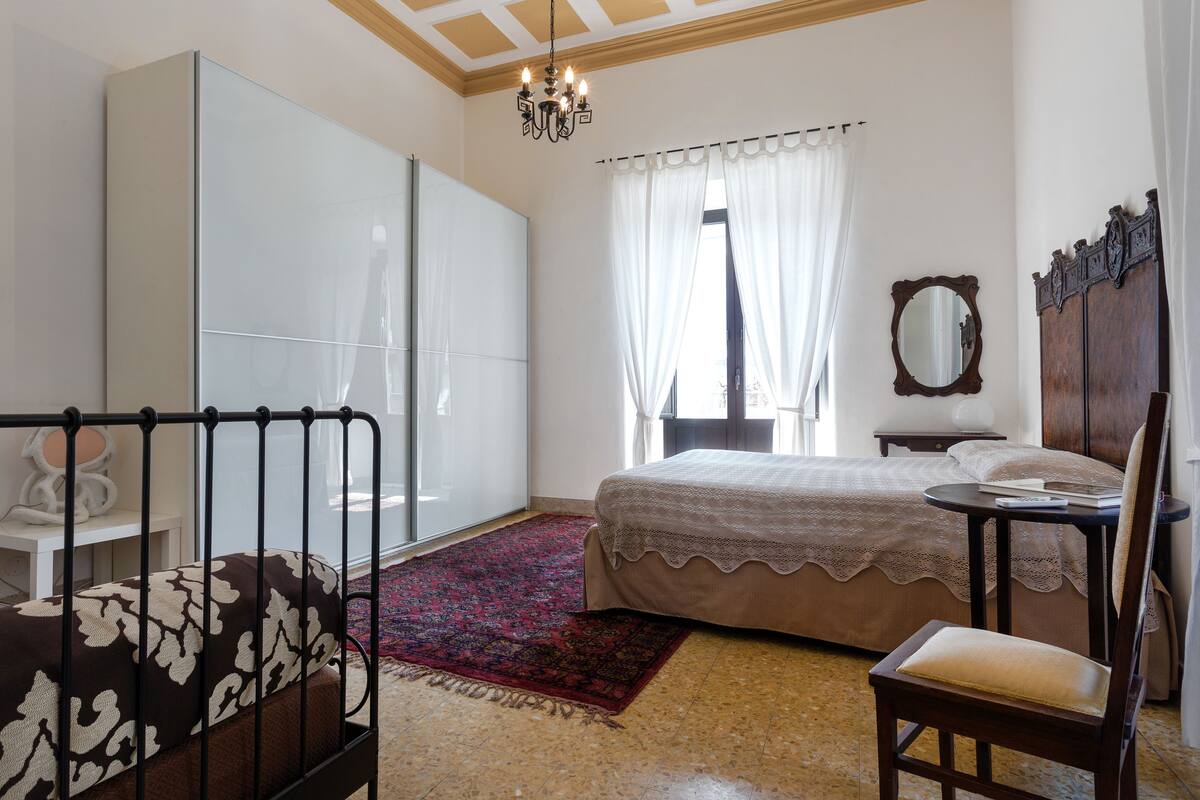 A bedroom with a bed, a chair, a desk, a wardrobe, and a mirror.