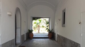 A corridor with white walls, a tiled floor, and two potted plants at the end. - Alcalà Living B&B (Catania)