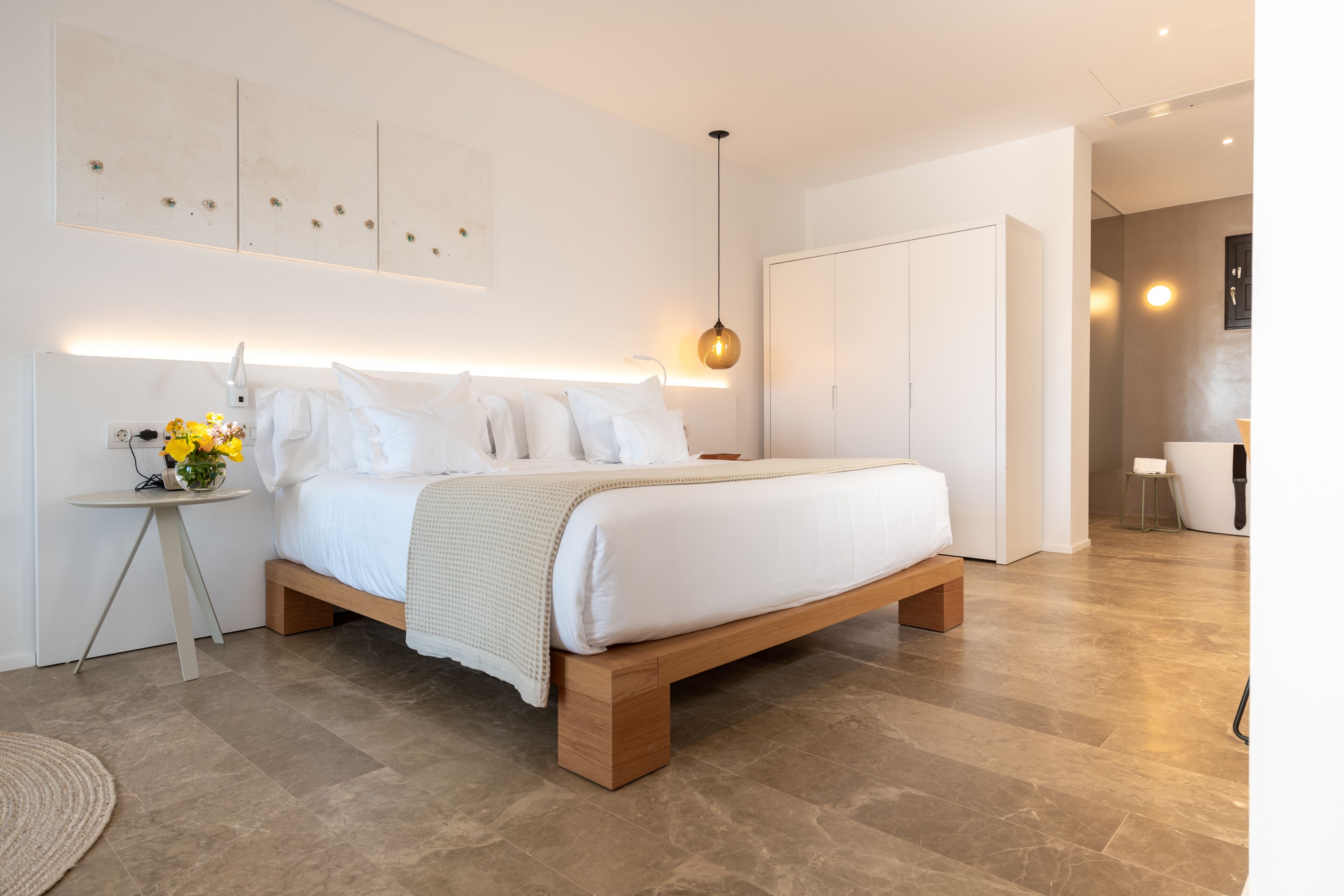 A modern bedroom with a large bed, bedside tables, a nightstand, and a wall-mounted light fixture.