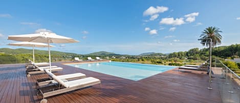 Una piscina al aire libre, sombrillas, sillones reclinables de piscina