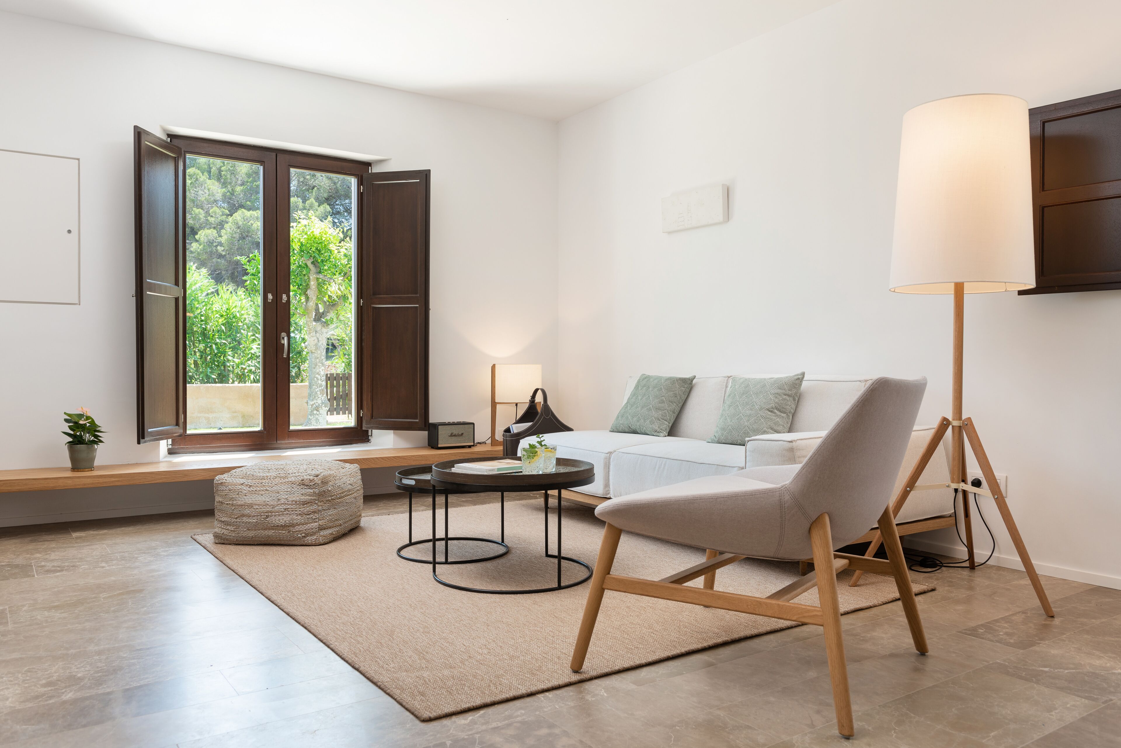 Een moderne woonkamer met een bank, voetenbankje, salontafel, vloerlamp en uitzicht door een glazen deur.