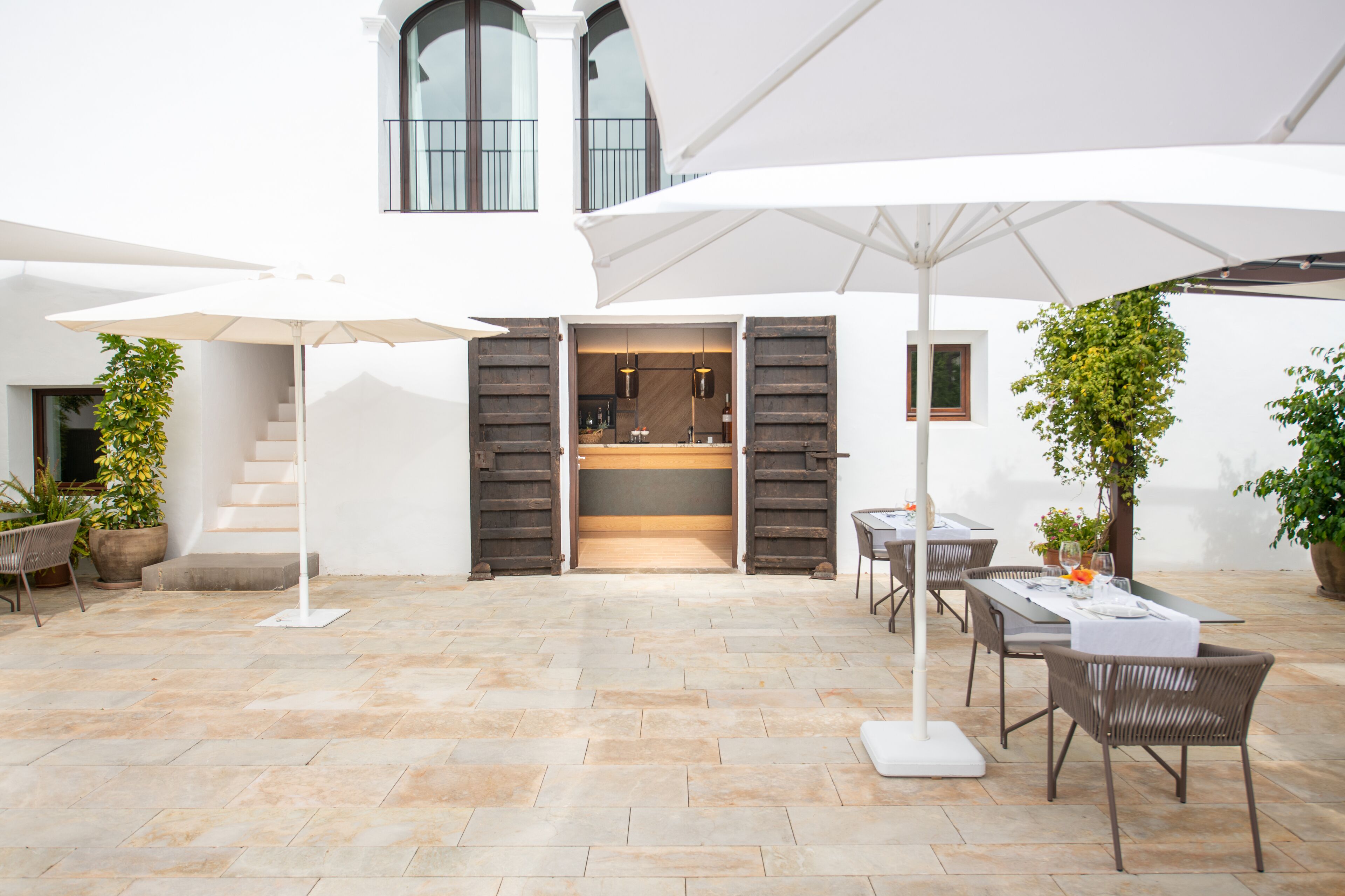 An outdoor patio with stone flooring, white umbrellas, wicker furniture, and potted plants.