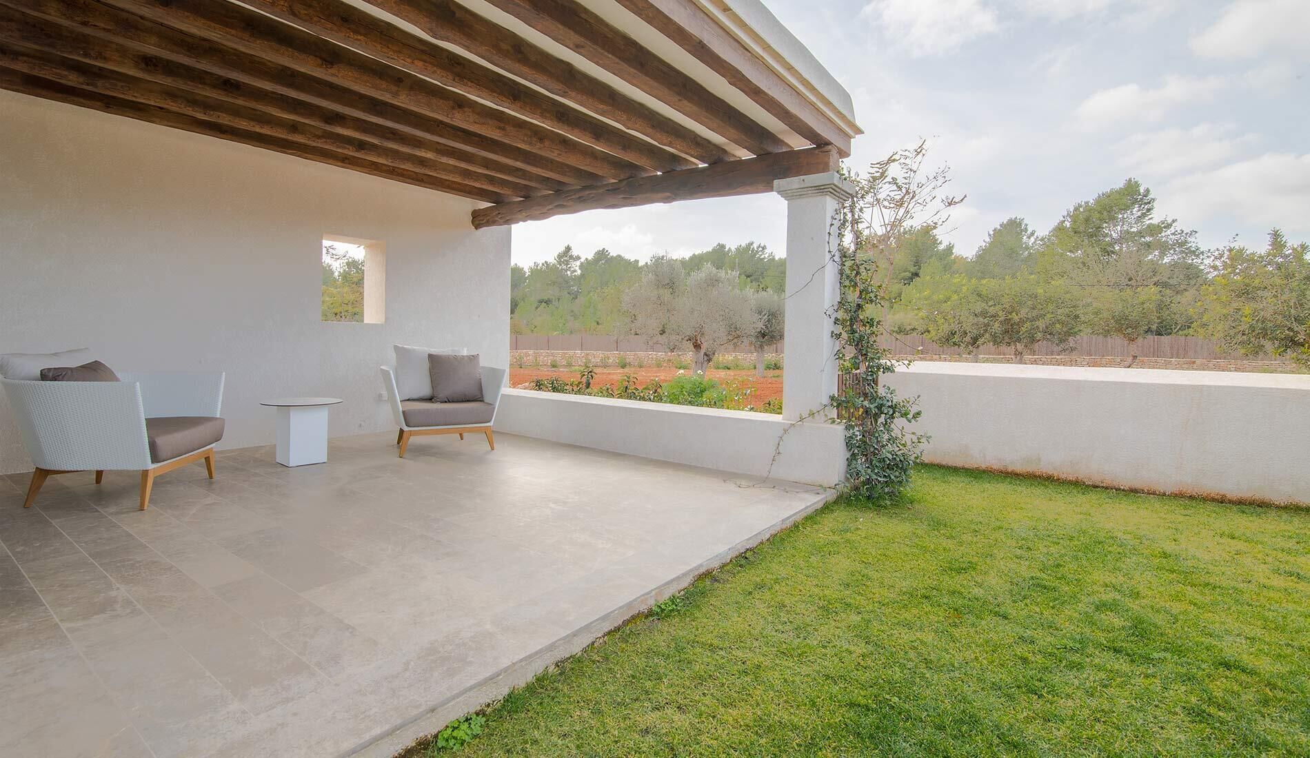 An outdoor patio with two chairs, a small table, and a view of a garden and trees.