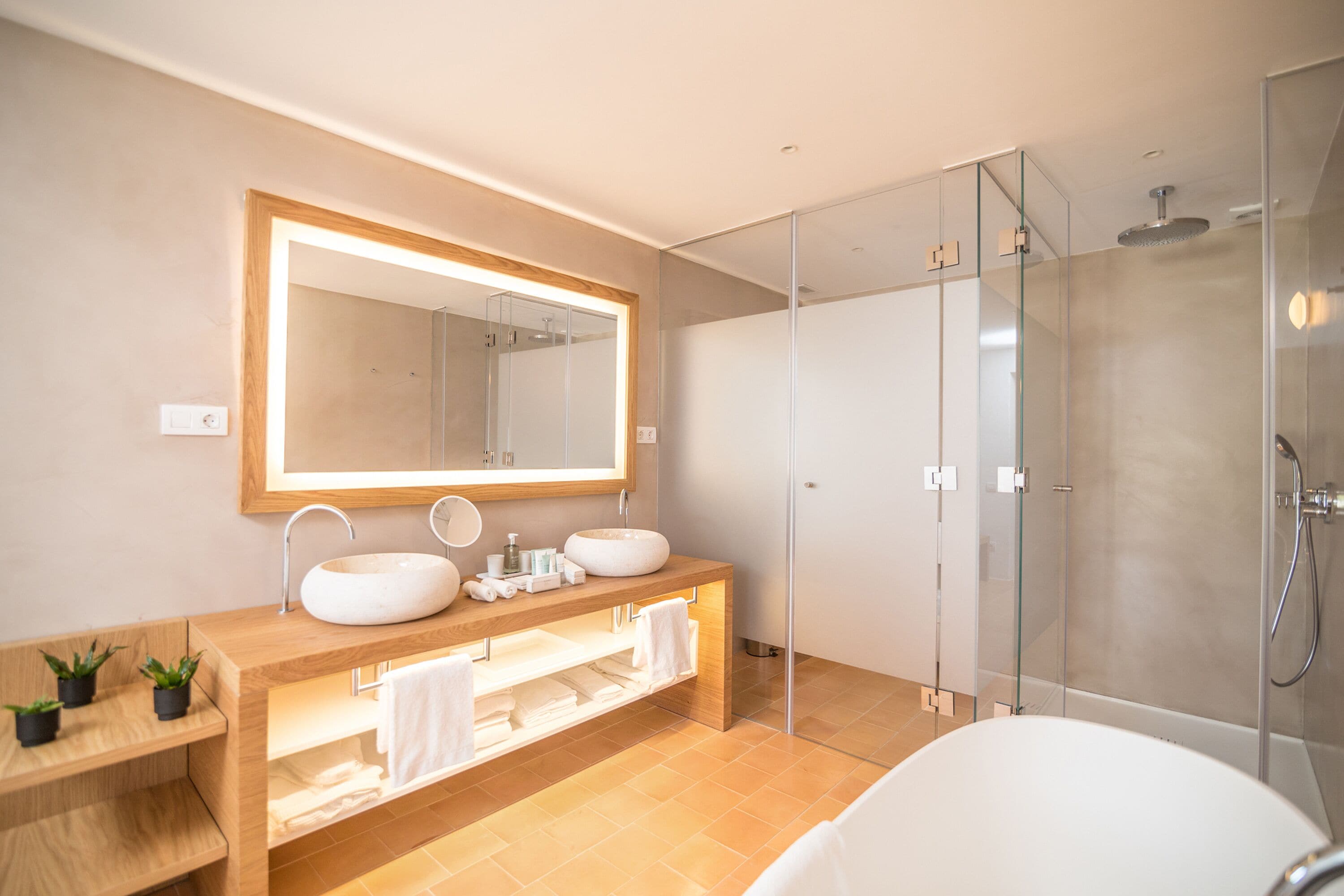 A modern bathroom with a large mirror, two sinks, a glass shower enclosure, and a bathtub.