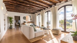 Un vaste espace de vie doté d’un plafond en bois, d’un canapé, d’une table basse et offrant une vue sur l’extérieur grâce à de grandes fenêtres.