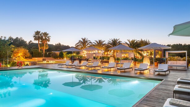 Une piscine entourée de palmiers et dotée d’une terrasse en bois, avec des chaises longues et des parasols.