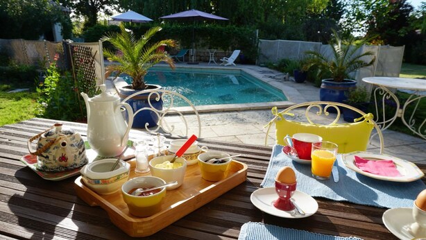 Desayuno dispuesto sobre una mesa de madera con diferentes platos y una bandeja, con vistas a una piscina.