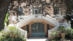 Un edificio con una escalera blanca que conduce a una puerta azul, rodeado de follaje y plantas en macetas.