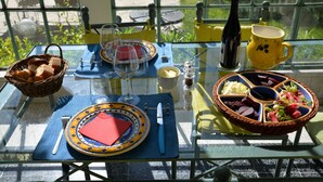 Una mesa de vidrio dispuesta con platos, cubiertos, una botella y una cesta de pan.