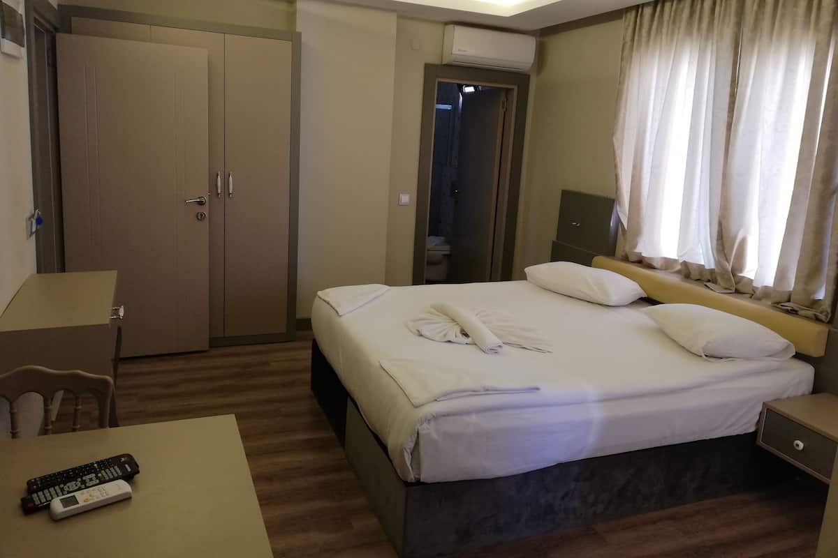 Habitación de hotel con cama, escritorio, silla, equipo de aire acondicionado y ventana con cortinas.