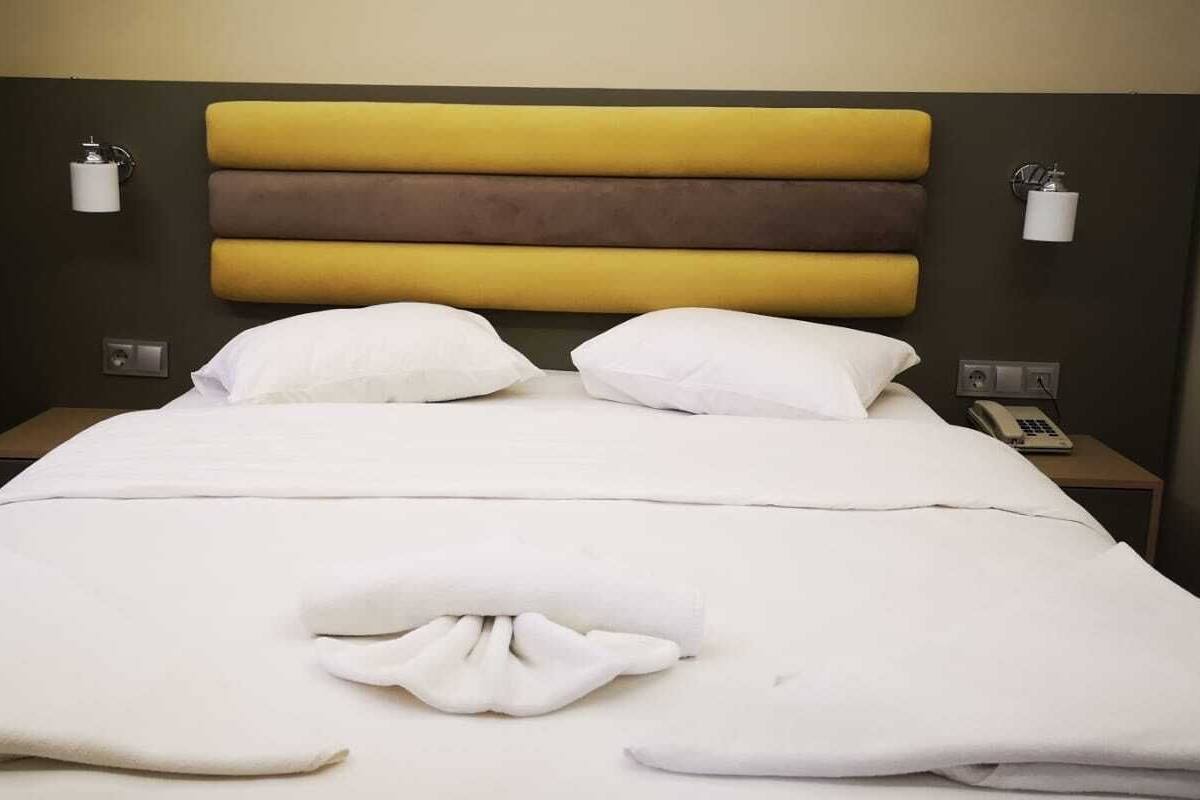 Habitación de hotel con una cama, dos mesitas de noche, un teléfono y una lámpara fijada a la pared.