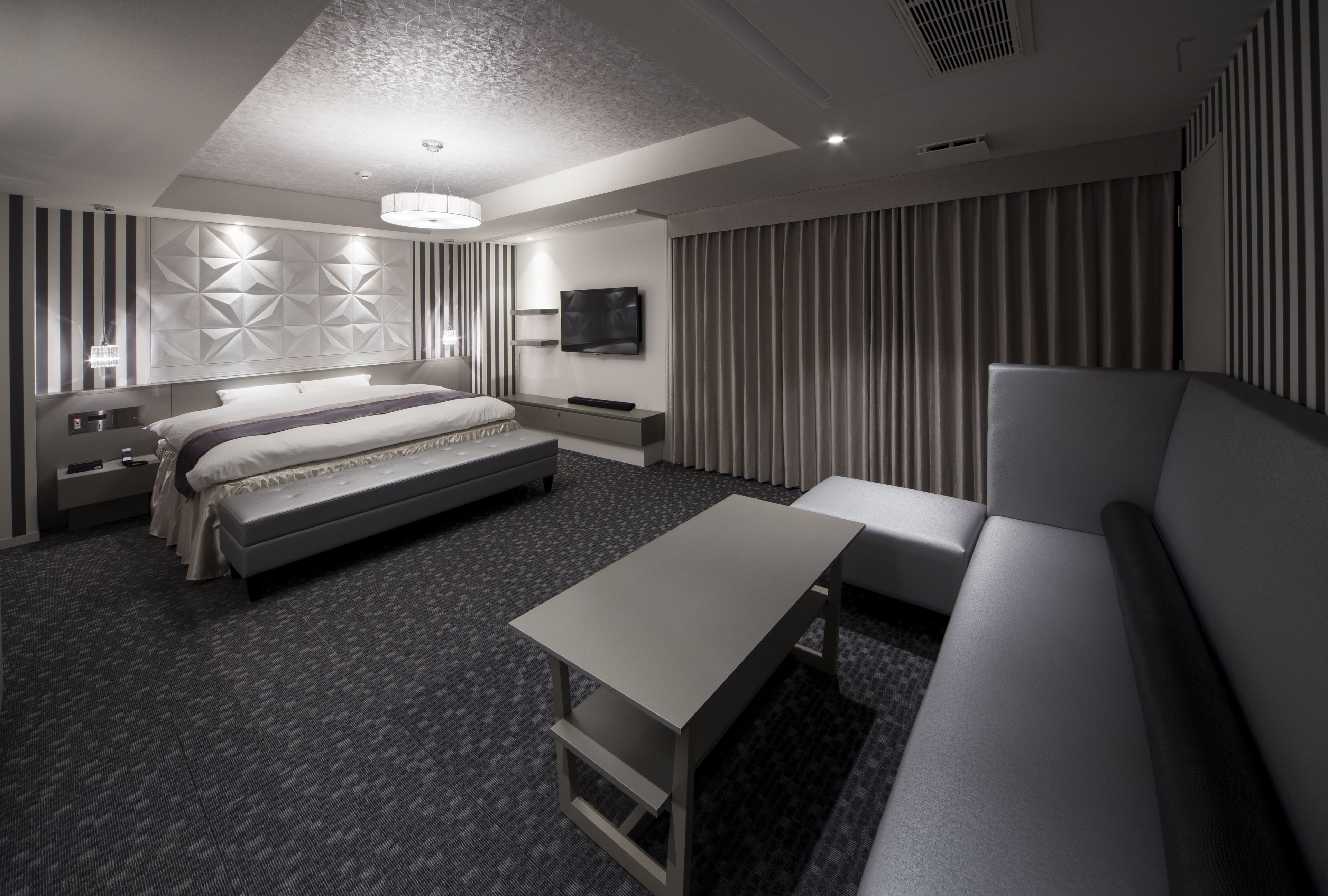A modern hotel room with a bed, a sofa, a TV, and a desk.