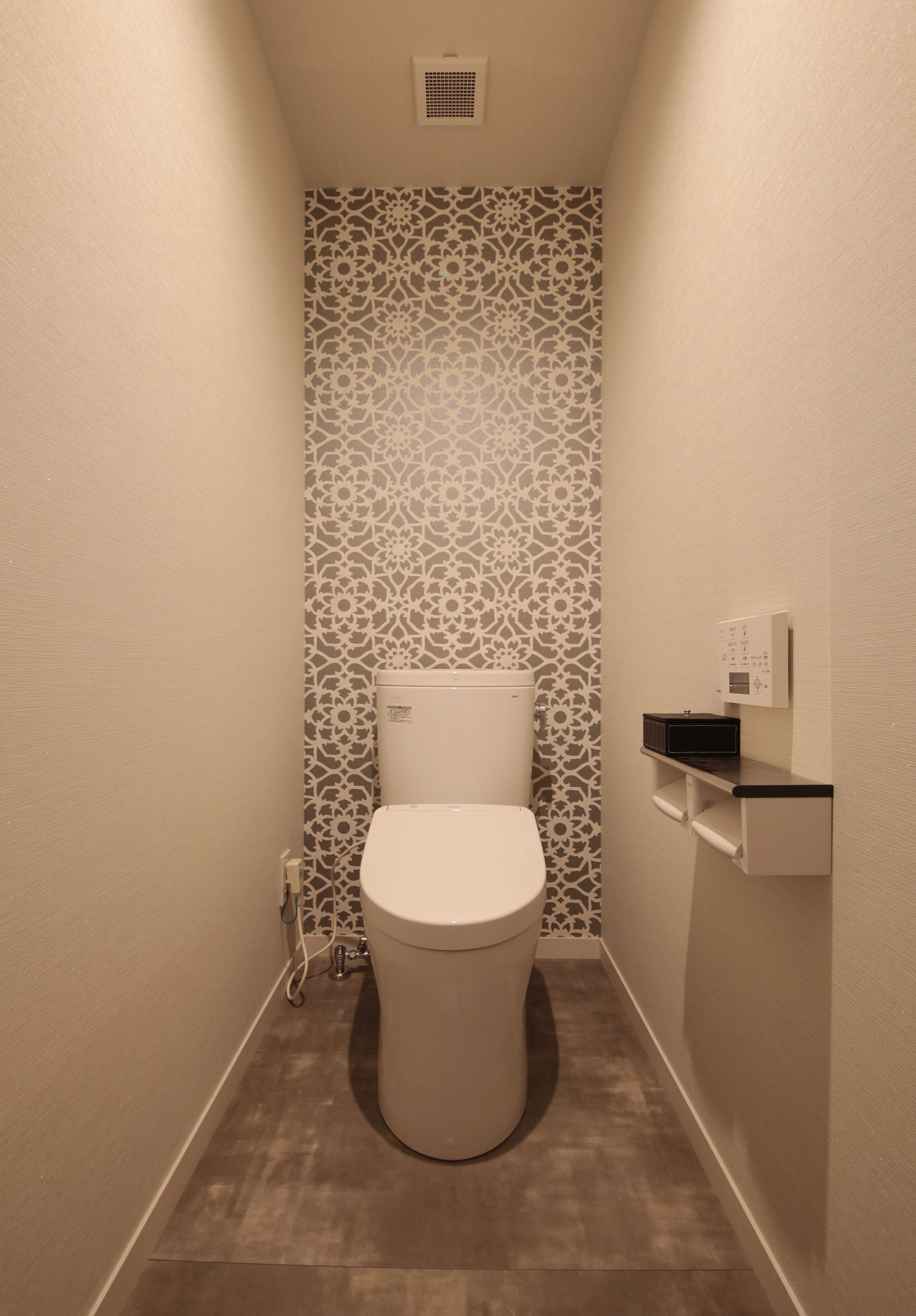 Un baño pequeño y estrecho con inodoro, un papel tapiz decorado y una repisa con panel de control.
