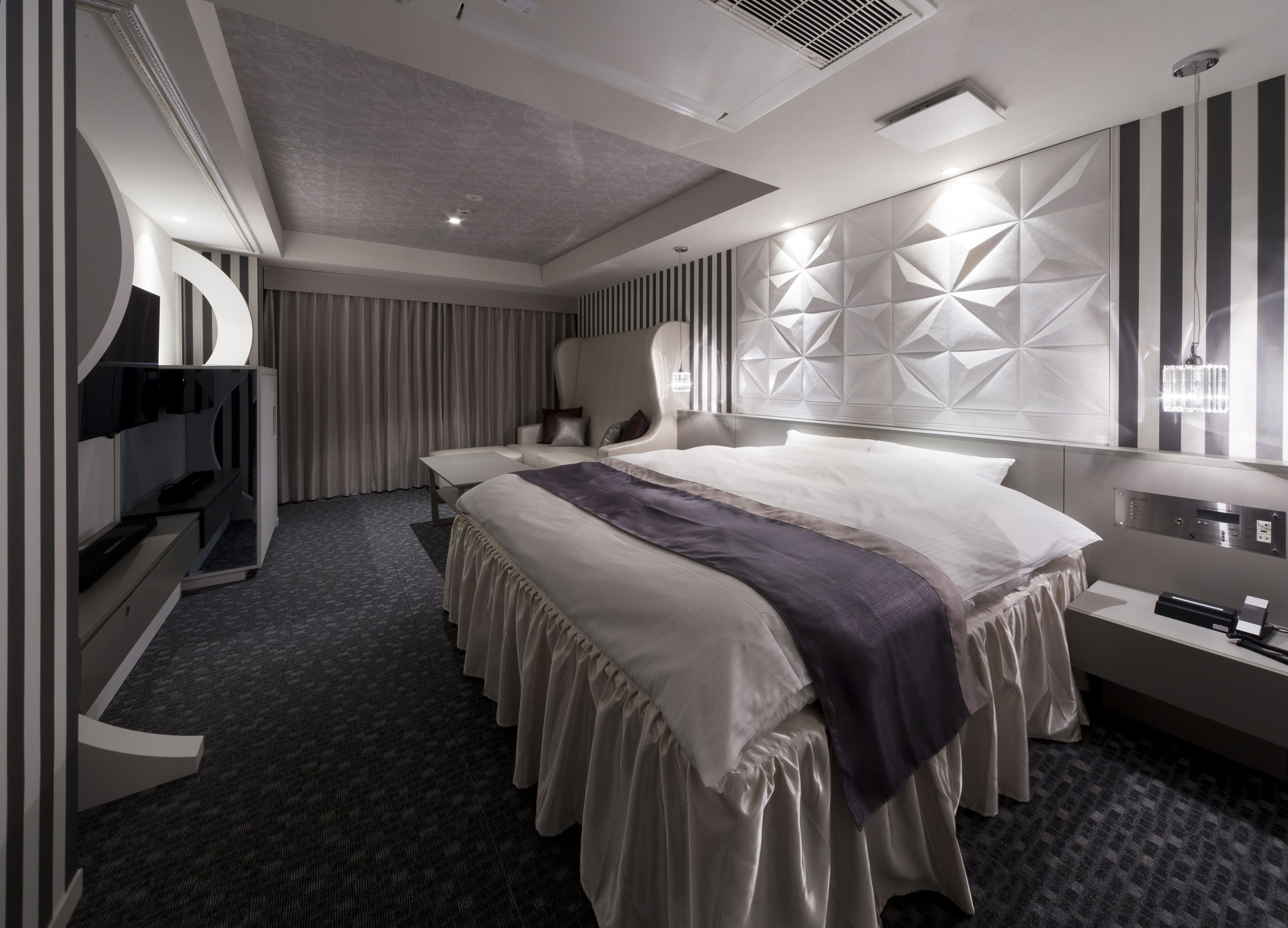 A modern hotel room with a large bed, a seating area, a TV, and a minibar.