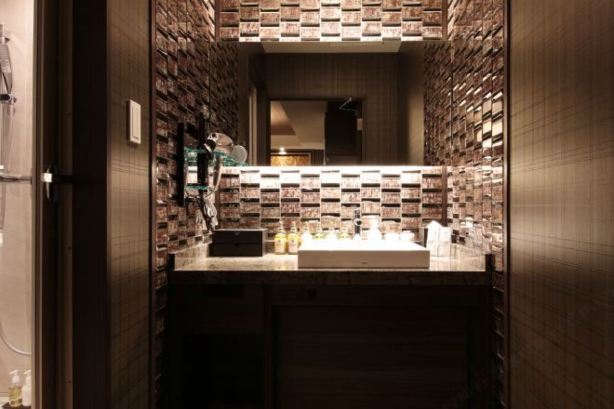 A modern bathroom with a brick-patterned wall, a large mirror, and a countertop with toiletries.