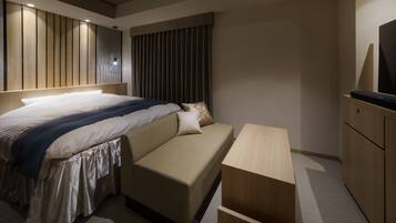 A modern hotel room with a large bed, a sofa, a wooden nightstand, and a TV.