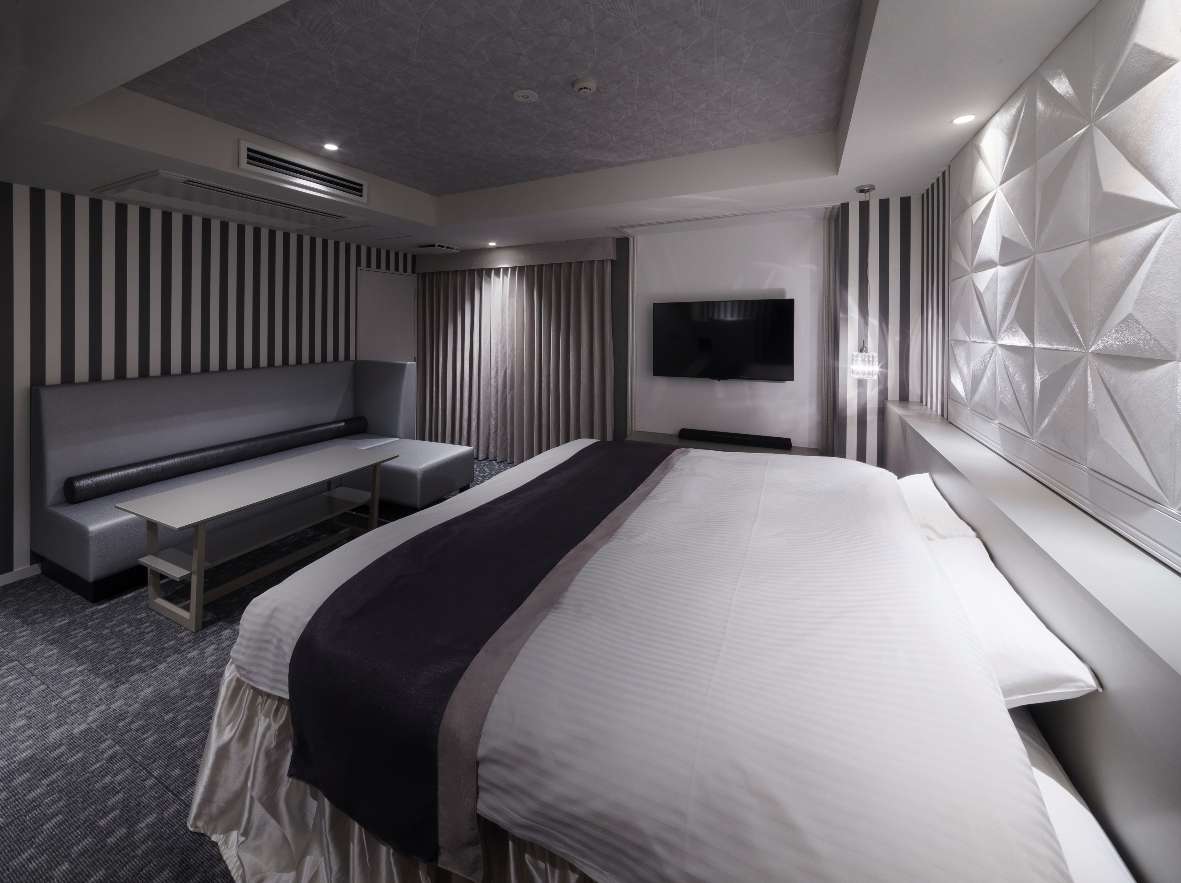 Ein modernes Hotelzimmer mit einem großen Bett, einer Sitzecke, einem Flachbildfernseher und einer dekorativen Wandverkleidung.