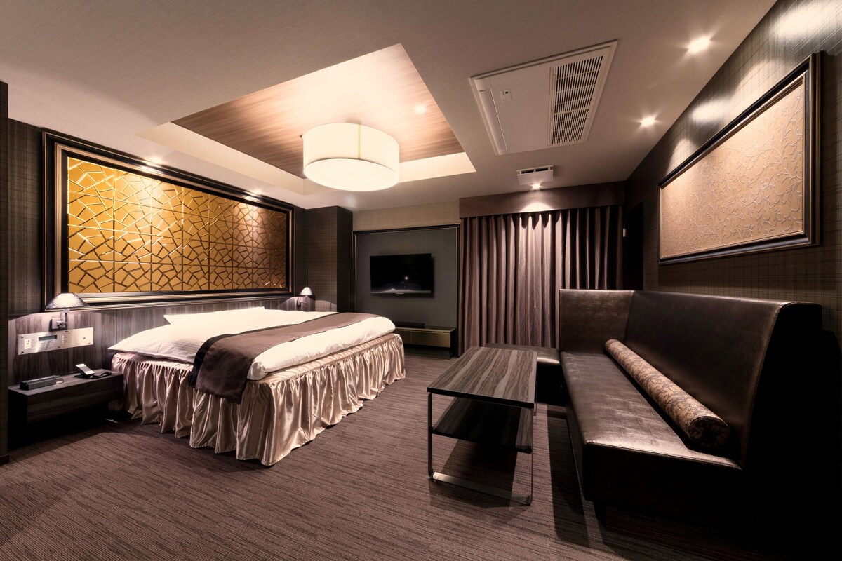 A modern hotel room with a large bed, a sofa, a flat-screen TV, and a decorative wall panel.