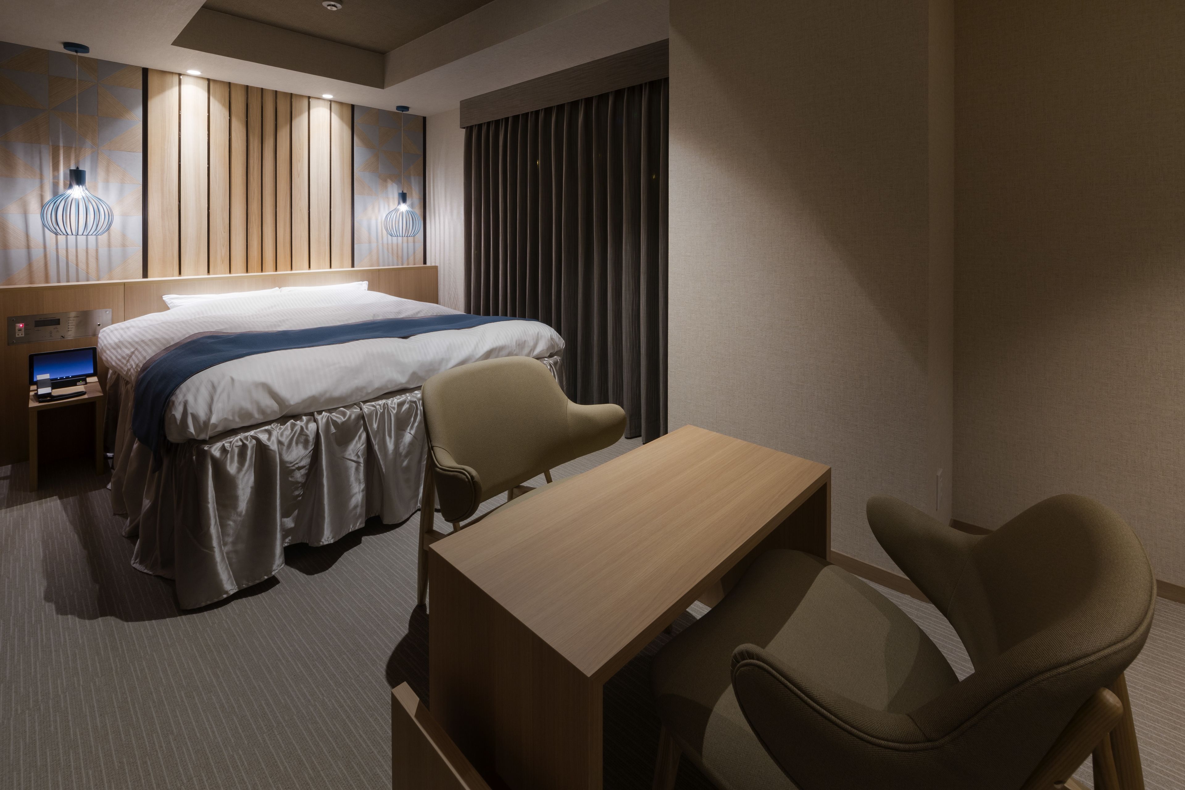 A hotel room with a bed, bedside table, lamp, and two chairs.