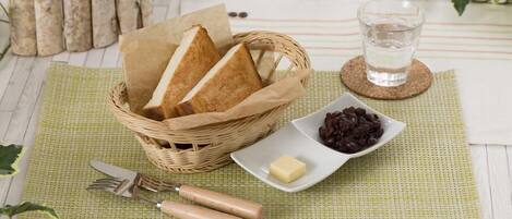 Een eettafel met een rieten mand vol brood, een klein bord met chocolade, een glas water en bestek op een groene placemat.
