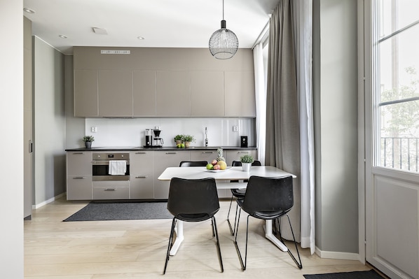 Una cocina moderna con gabinetes grises, una encimera blanca y un área de comedor con dos sillas negras.