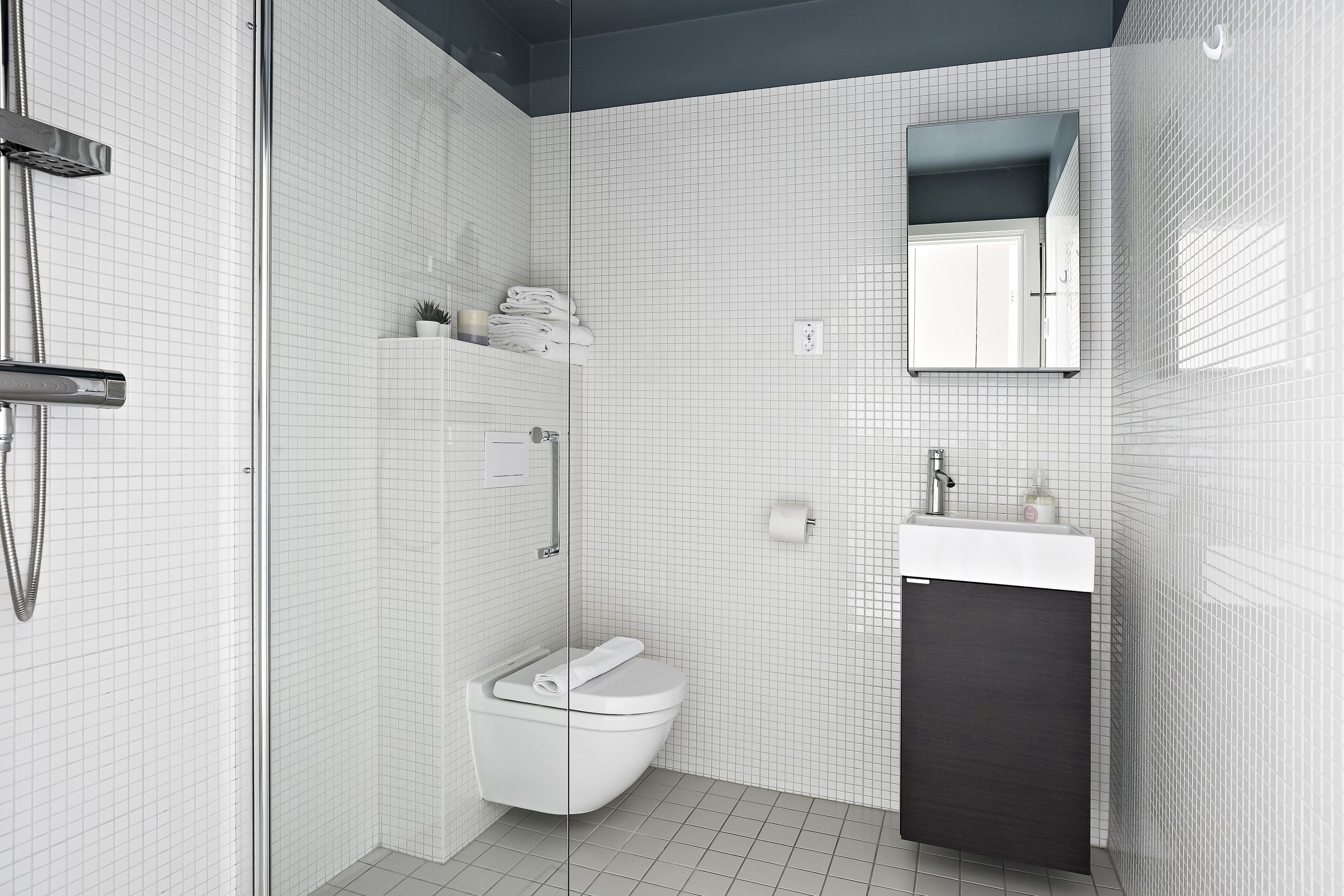 Un bany modern amb un espai de banyera de vidre, un vàter blanc, un moble de bany fosc i un mirall sobre el lavabo.