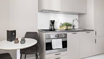 A modern kitchen with a built-in oven, a coffee maker, and a sink. There is a round table with chairs and a potted plant on the counter.