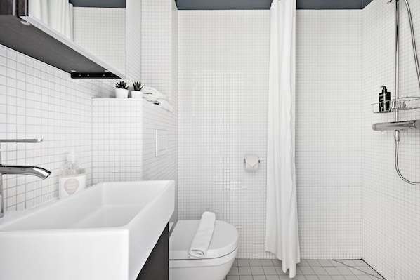 Un baño moderno con lavamanos, inodoro y zona de ducha, todo en blanco.