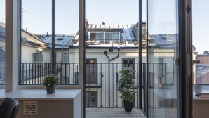 A balcony with a view of neighboring buildings, a potted plant, and a window with a metal grill. - Forenom Apartments Stockholm Johannesgatan (Stockholm)