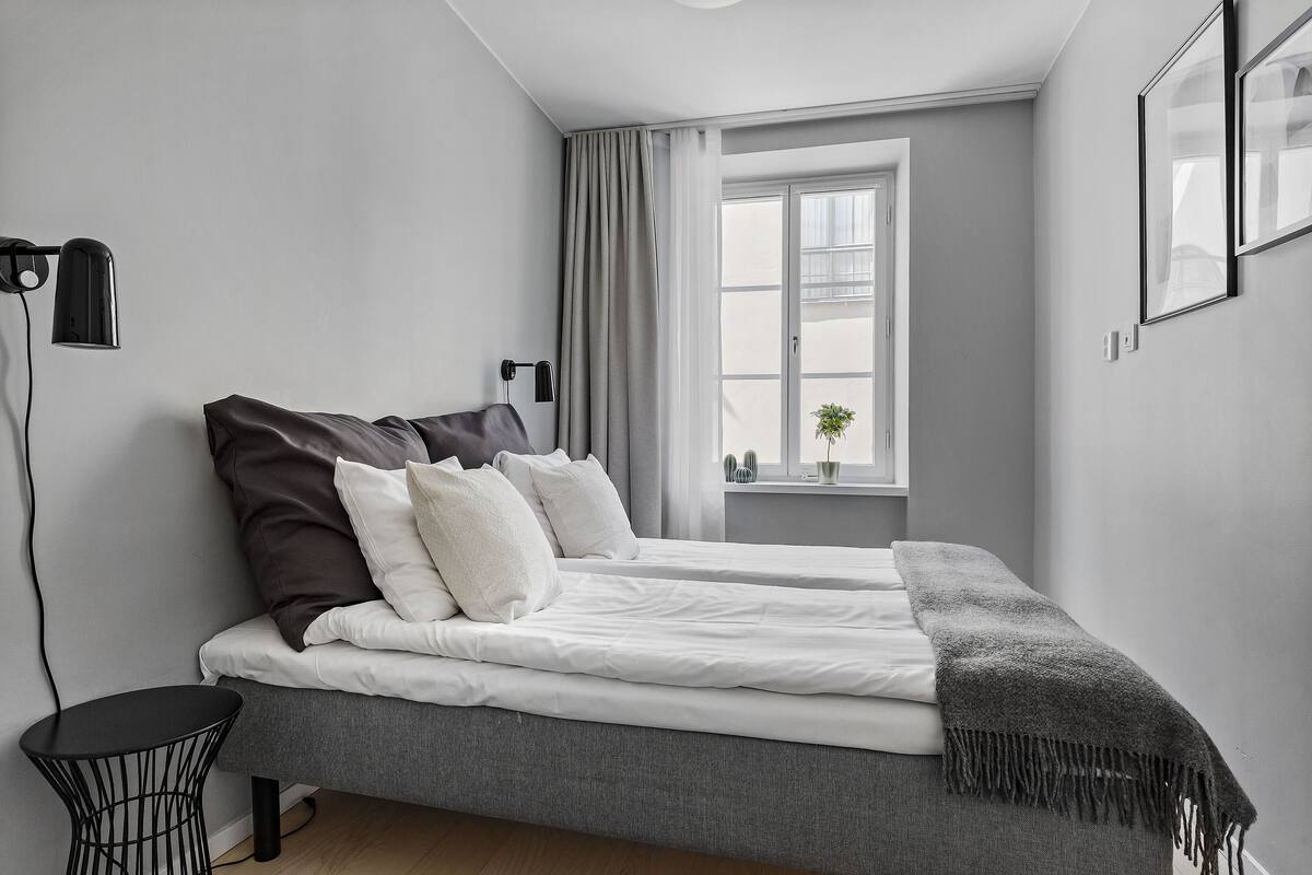 Um quarto moderno com cama, mesas de cabeceira, janela com cortinas e uma planta.