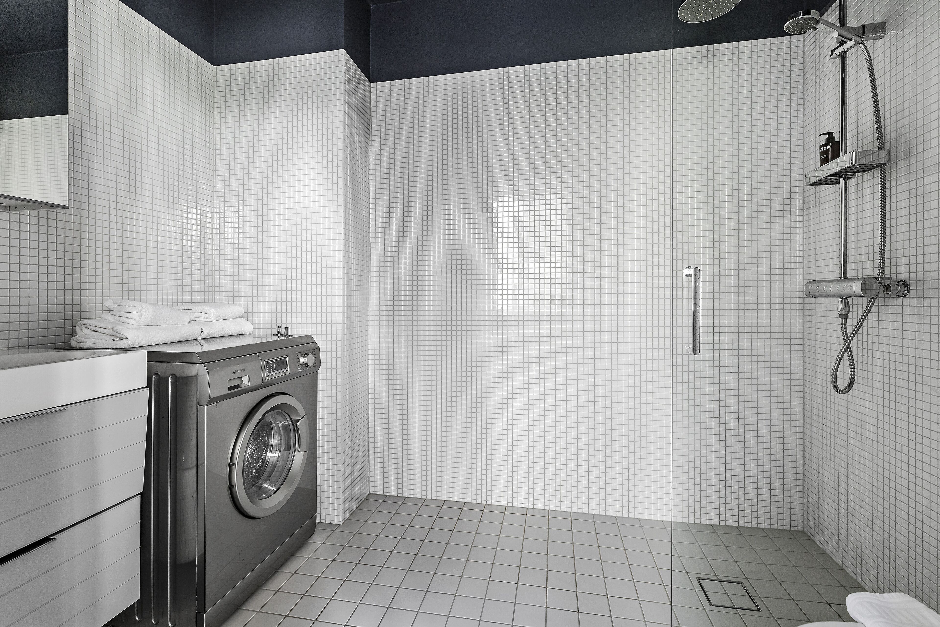 A modern bathroom with a washing machine, a shower, and a tiled floor.
