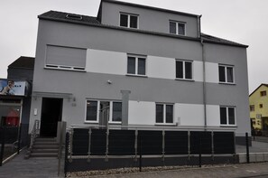 A multi-story residential building with a grey facade, white horizontal stripes, and a black fence in front. - Ebersheim Luxus Plaza (Mainz)