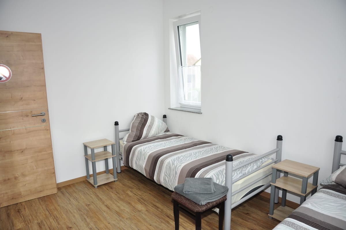 A bedroom with a single bed, a small table, a chair, and a window.
