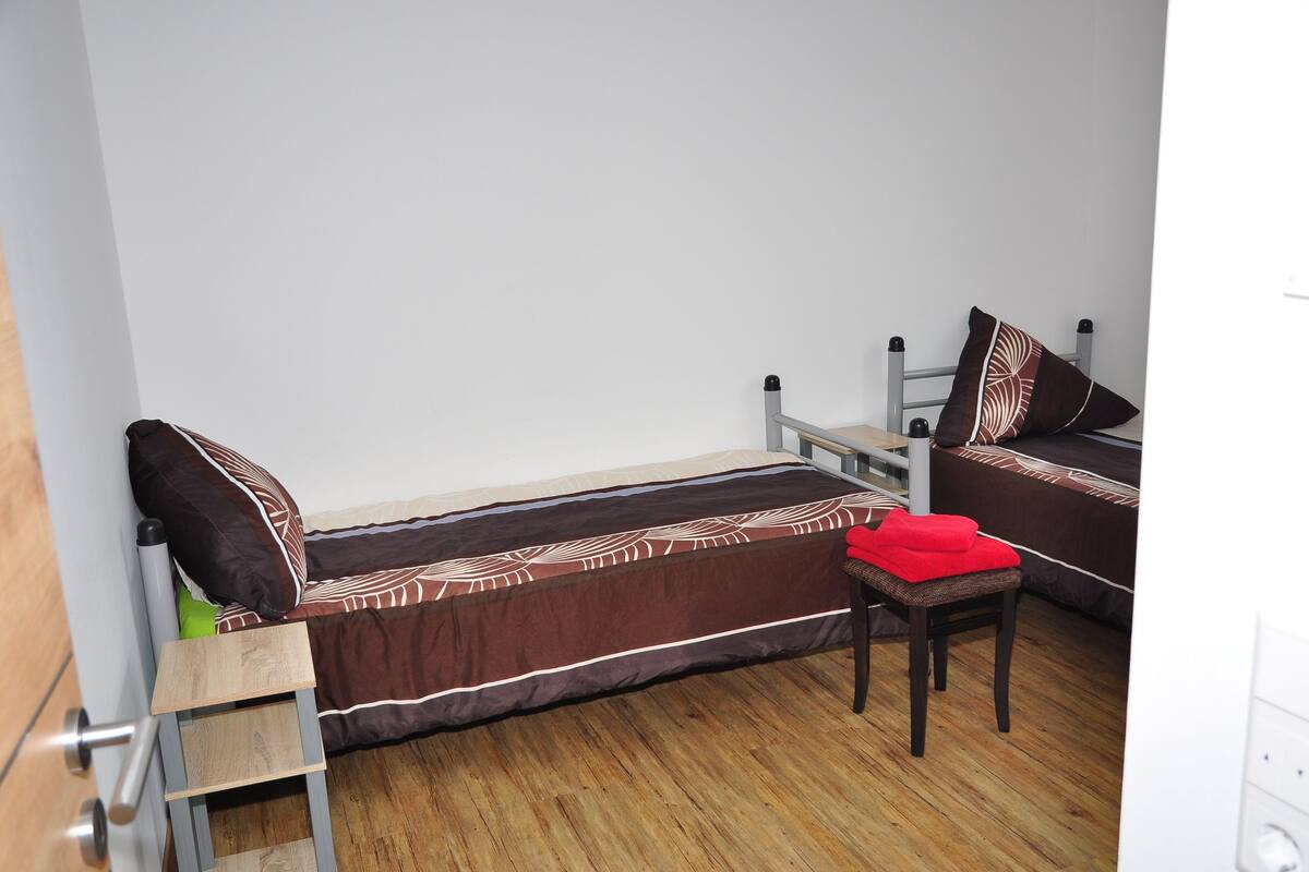 A small, compact room with a single bed, a wooden chair, and a small table.