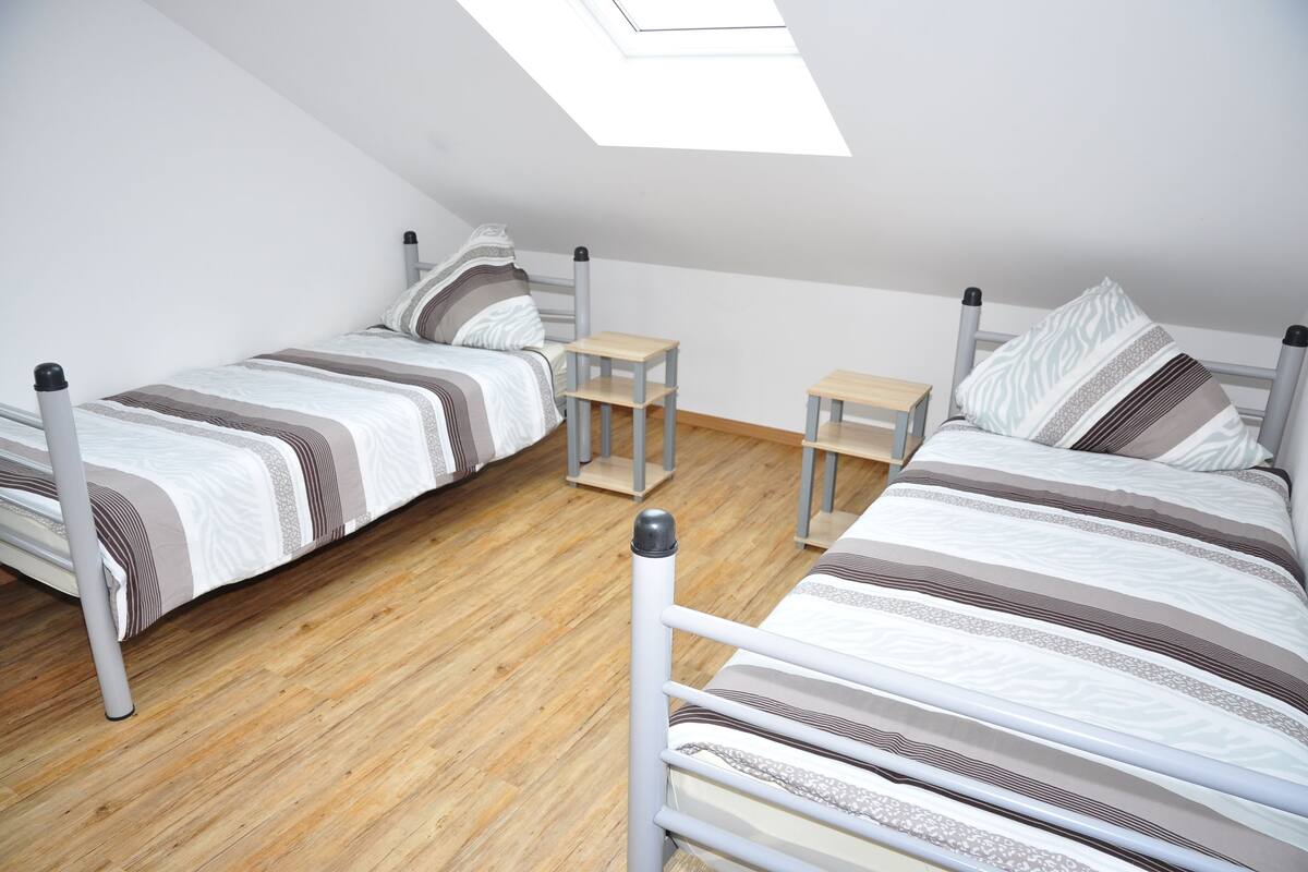 A dormitory room with two single beds, a skylight, and a small wooden table.