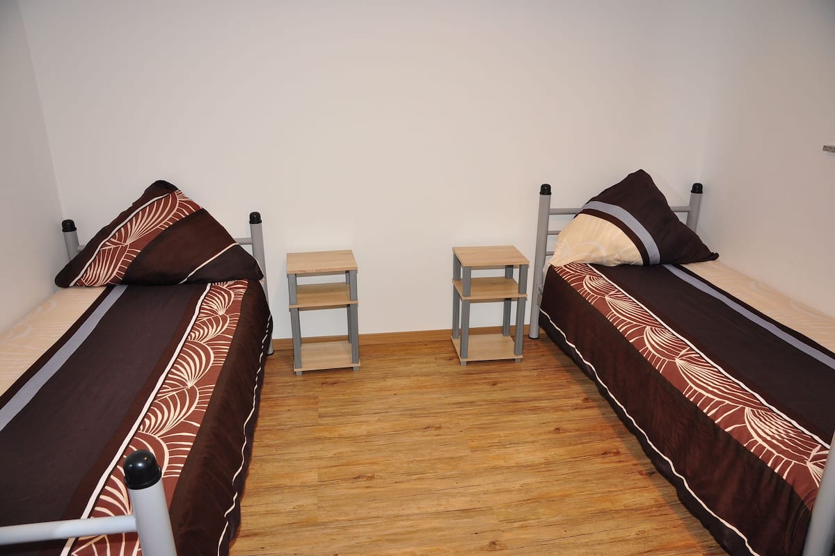 A room with two single beds, each with a wooden nightstand.