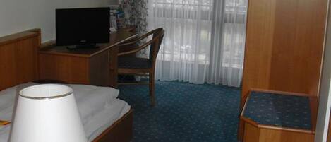 A hotel room with a bed, a desk, a television, a lamp, a telephone, and a wardrobe.