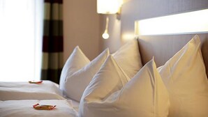 Un lit bien fait, avec des oreillers blancs et un rideau à rayures en arrière-plan.