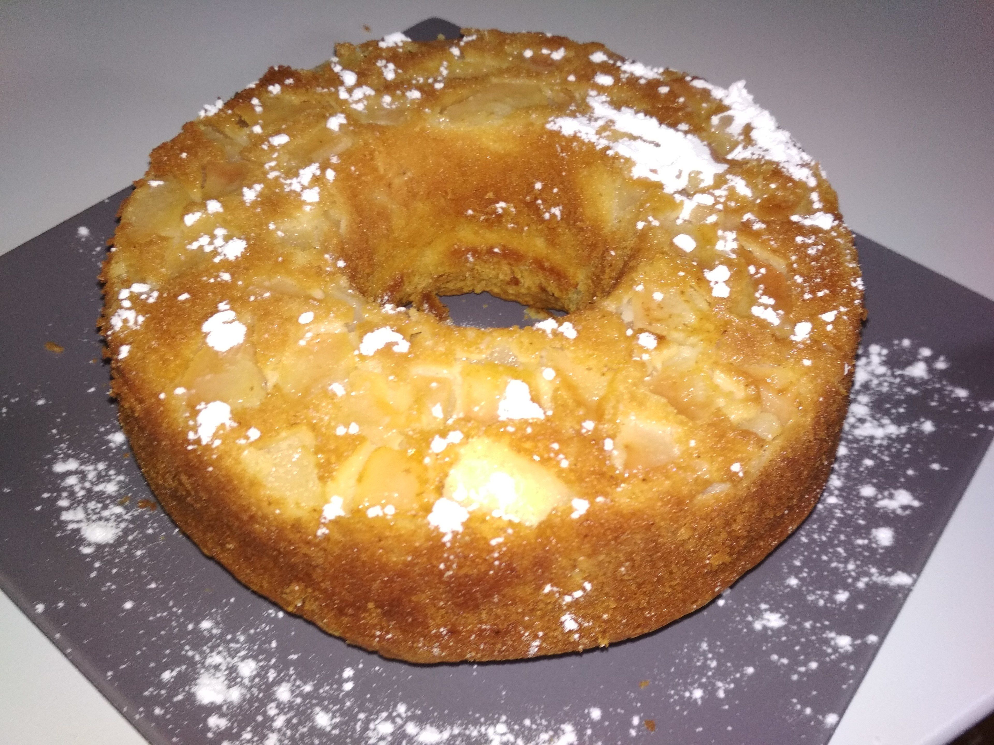 Ein runder, goldbrauner Kuchen mit Puderzucker auf einem Teller.