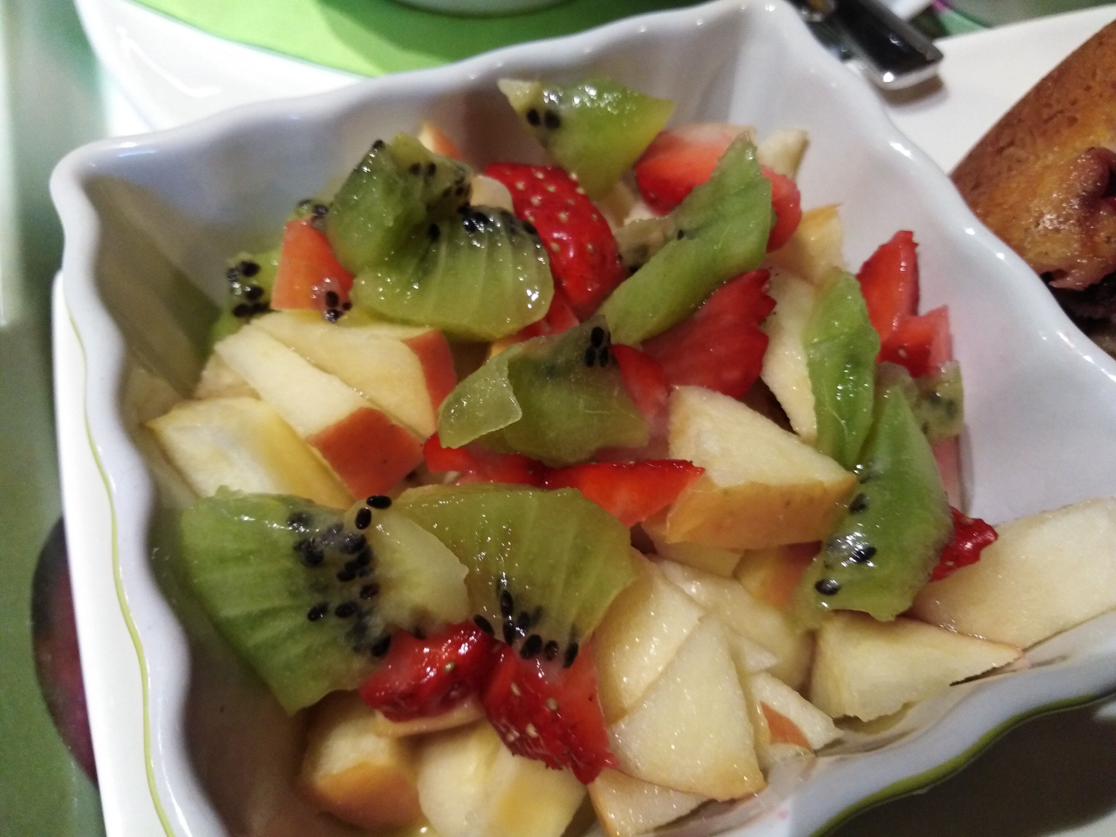 A white bowl filled with assorted fruits including kiwi, strawberries, and apples.