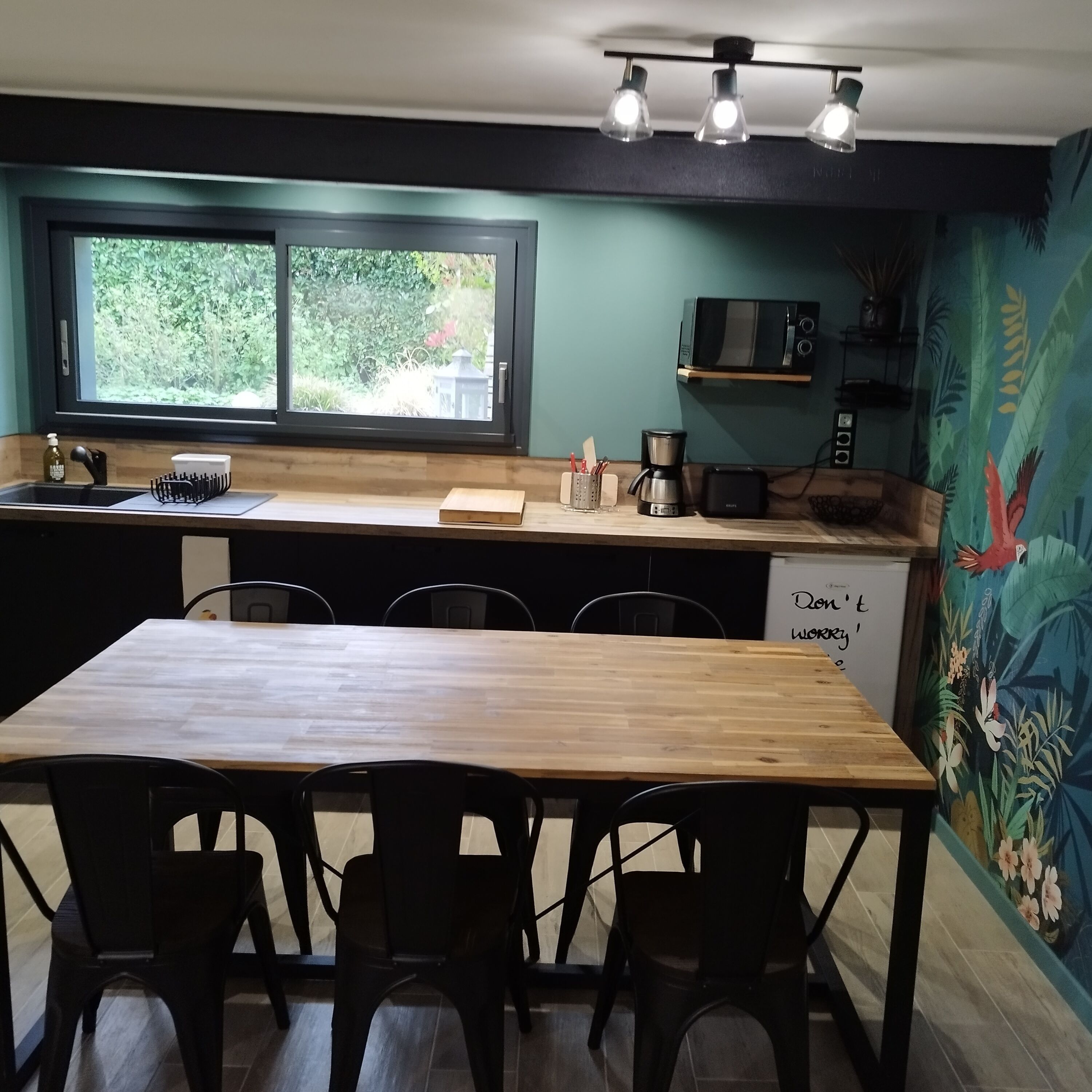 A kitchen with a wooden table and chairs, a window, a microwave, and a coffee maker.