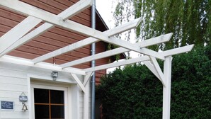 Een houten terras met een pergola, een stoel en bloemenbakken.