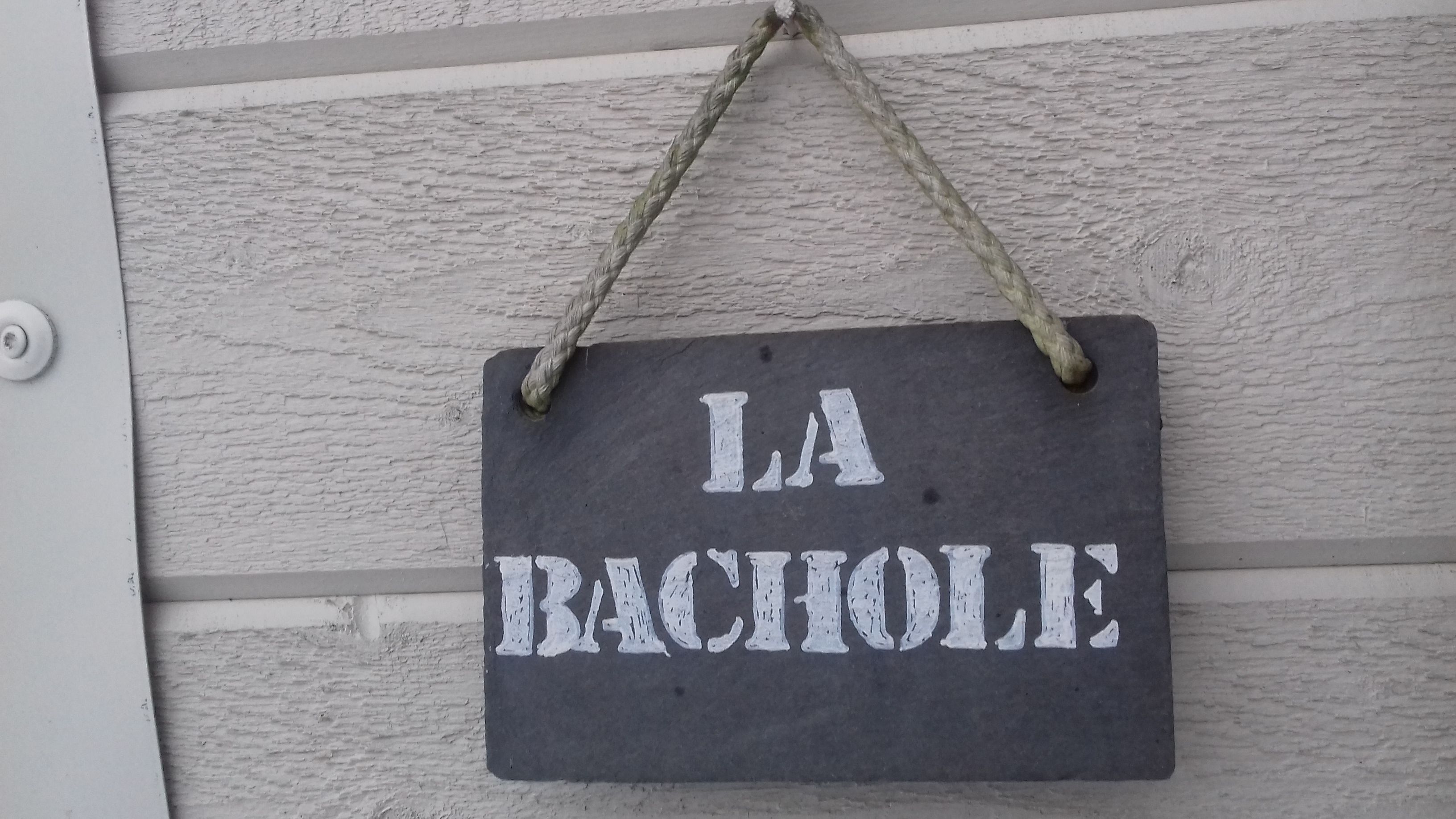 Une plaque d’ardoise portant l’inscription « LA BACHOLE » est accrochée à un mur à la texture particulière.