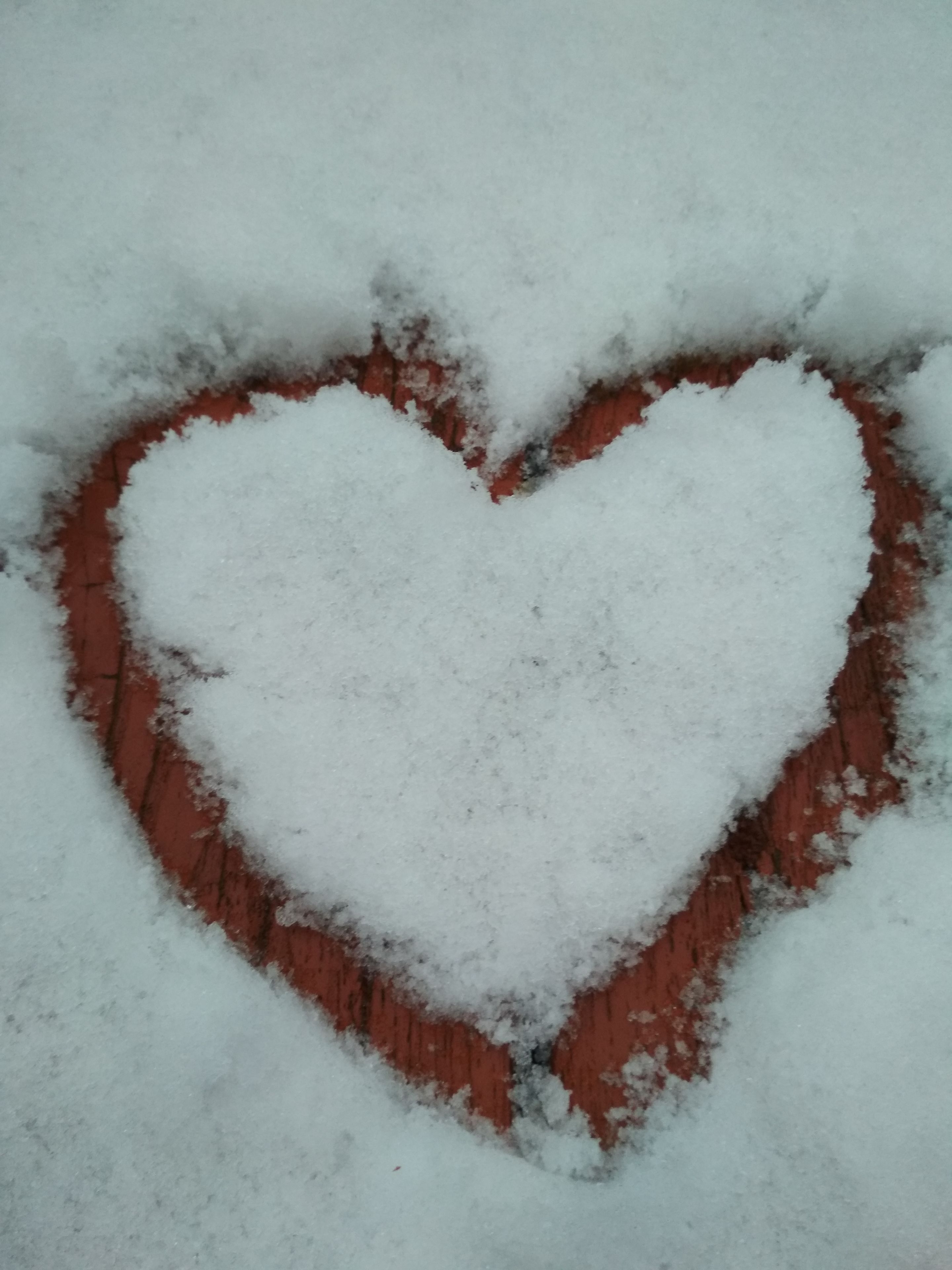 Un motif en forme de cœur réalisé dans la neige sur une surface en briques.