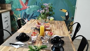 Een houten eettafel met ontbijtartikelen, een plant en een muurschildering van een tukan en palmbladeren.
